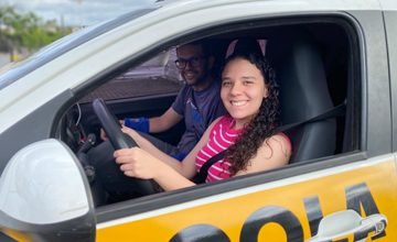 Aluna sorridente ao volante, com o instrutor ao lado
